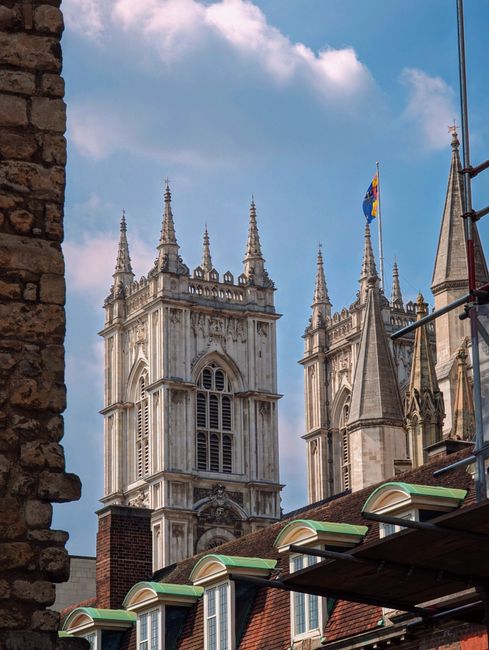 Close-up view of the exterior stone facade of Westminster Abbey, showcasing intricate Gothic architecture with pointed arches, detailed tracery, and tall pinnacles. The facade features a mix of light-